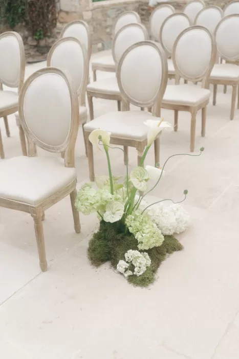 Cream ceremony chairs with soft green and white aisle flowers at Mas Torroella.