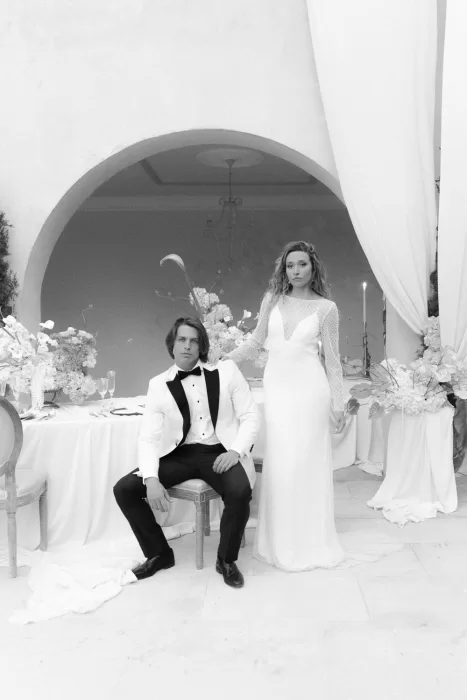 Editorial-style black and white portrait of the couple in front of floral reception table at Mas Torroella.
