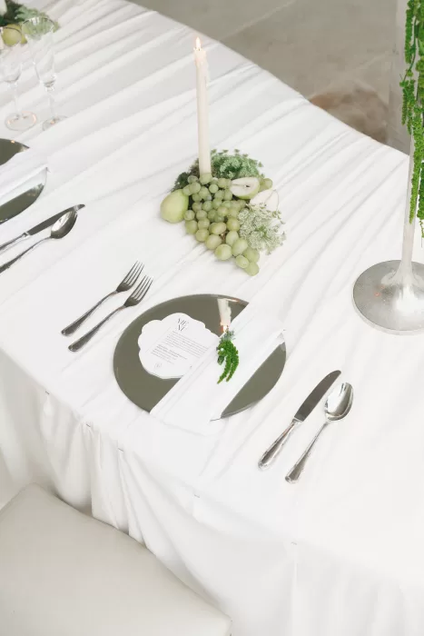 Elegant modern wedding table setting at Mas Torroella with white draping, mirrored chargers, and green fruit details.