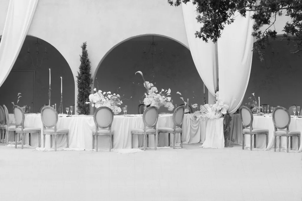 Black and white image of a romantic reception setup with florals and draped arches at Mas Torroella.