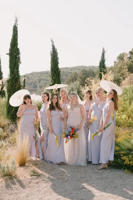 Bride surrounded by her bridesmaids with parasols and yellow calla lilies at Masia Cabellut