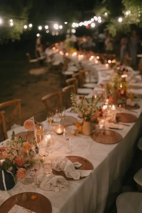 Warm candlelight and empty wine glasses on a long dinner table under string lights at Masia Cabellut