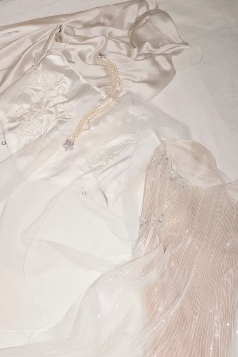 Flat lay of embroidered bridal gowns and pearl necklace on a white bedspread at Masia Cabellut