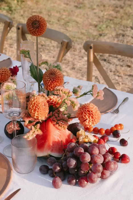 Vibrant table centerpiece with orange dahlias, watermelon, and grapes at Masia Cabellut