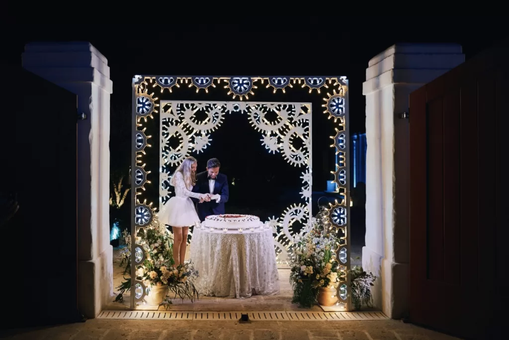 Bride and groom cutting the wedding cake under a light installation at Masseria Calderisi