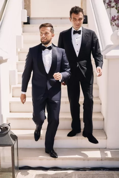 Groom and groomsman descend the white stone staircase in classic tuxedos at Masseria Calderisi