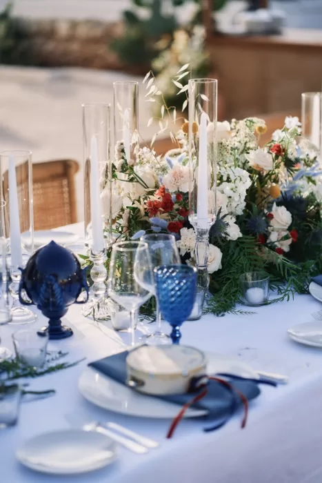 Lush floral centrepiece and blue glassware on sunlit reception table at Masseria Calderisi