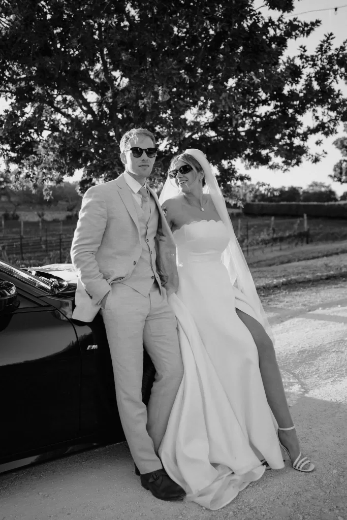 Cool and editorial black-and-white portrait of the newlyweds by their car under the trees at Masseria Monitilli.