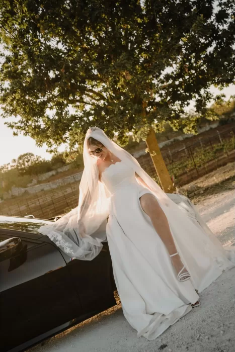 The bride stepping gracefully out of a black convertible in golden light, her veil flowing behind her at Masseria Monitilli.