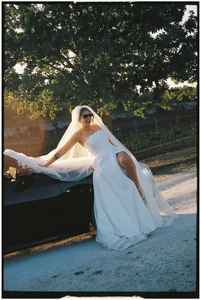 The bride laughing joyfully while leaning on a black convertible at Masseria Monitilli.
