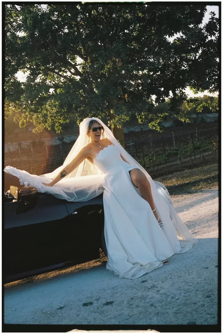 The bride laughing joyfully while leaning on a black convertible at Masseria Monitilli.