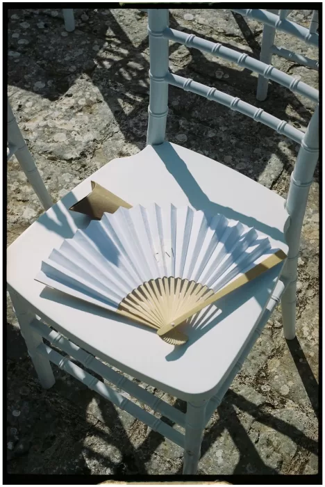 A white paper fan placed on a ceremony chair under the Apulian sun at Masseria Monitilli.