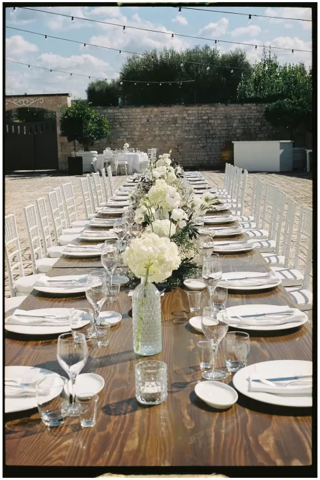 A long reception table lined with white flowers and crystal glassware in the courtyard at Masseria Monitilli.