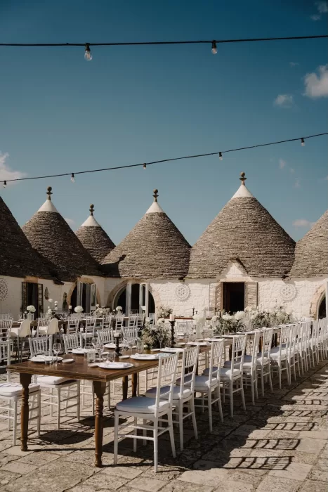 Outdoor reception setup under festoon lights with trullo rooftops at Masseria Monitilli.