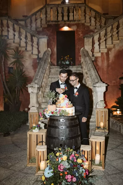 Grooms cutting a colorful wedding cake surrounded by lanterns at Masseria Spina.