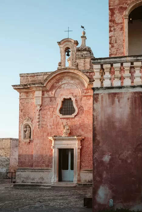 Romantic pink-hued exterior of Masseria Spina with detailed statues and soft sunset lighting