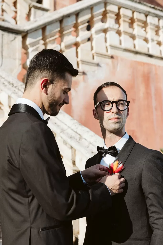 One groom adjusting the other’s boutonnière in the sunlit courtyard of Masseria Spina