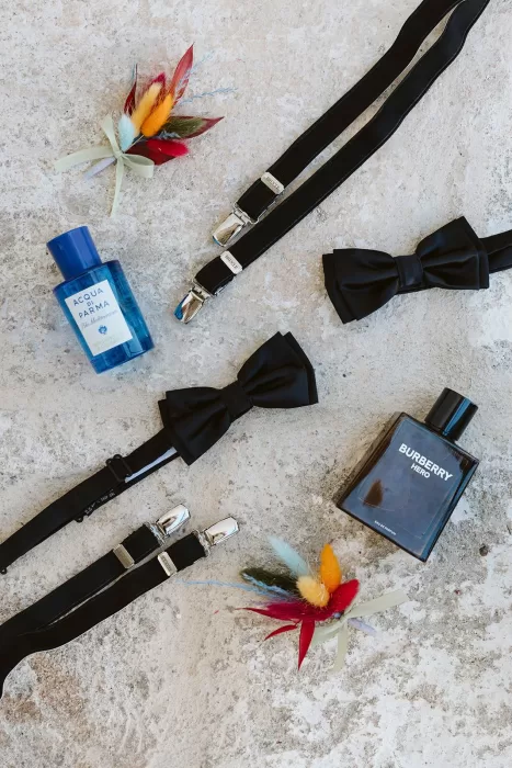 Flatlay of bow ties, suspenders, cologne, and boutonnières for a wedding at Masseria Spina