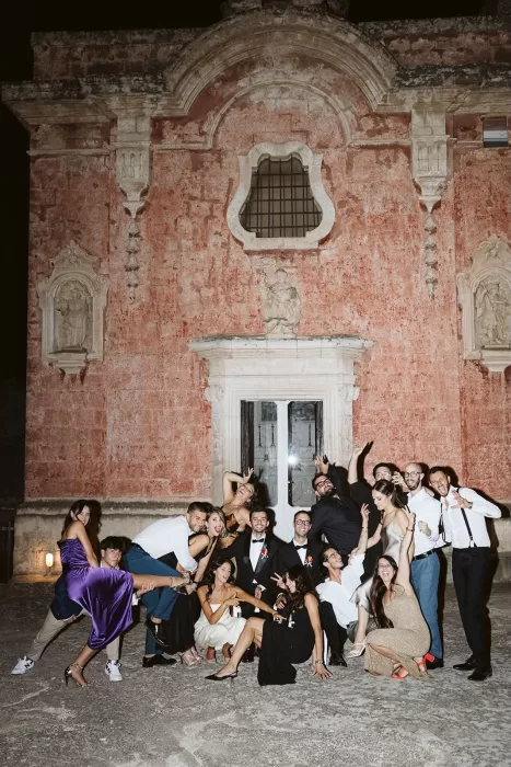 Group of guests celebrating joyfully outside the red facade of Masseria Spina at night.