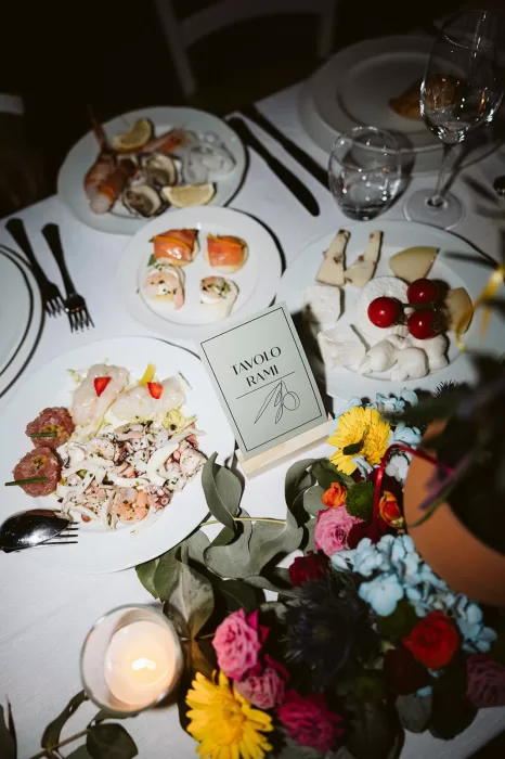 A colourful wedding table at Masseria Spina featuring seafood starters, artisan cheeses, floral centrepieces, and a "Tavolo Rami" table sign.