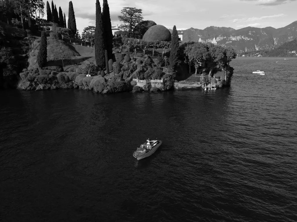 Aerial view of a wooden boat on Lake Como near the iconic trees and shoreline of Parco Civico Teresio.