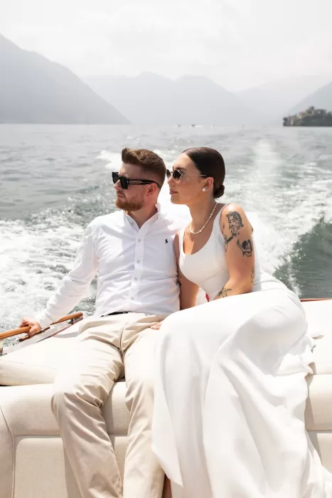 Bride and groom seated on a boat on Lake Como, gazing across the water near Parco Civico Teresio.