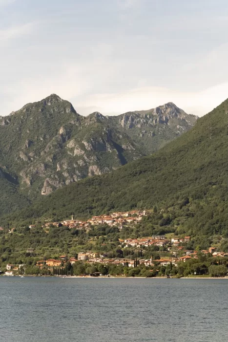 Distant view of a quiet lakeside village nestled against the mountains, captured from Parco Civico Teresio.