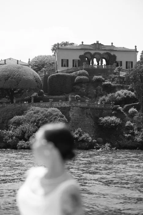 Bride gazing from the water toward an ivy-covered villa terrace near Parco Civico Teresio, captured in dreamy black and white.