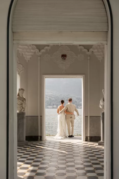 Couple standing in an arched villa corridor at Parco Civico Teresio, looking out over Lake Como through an open doorway.