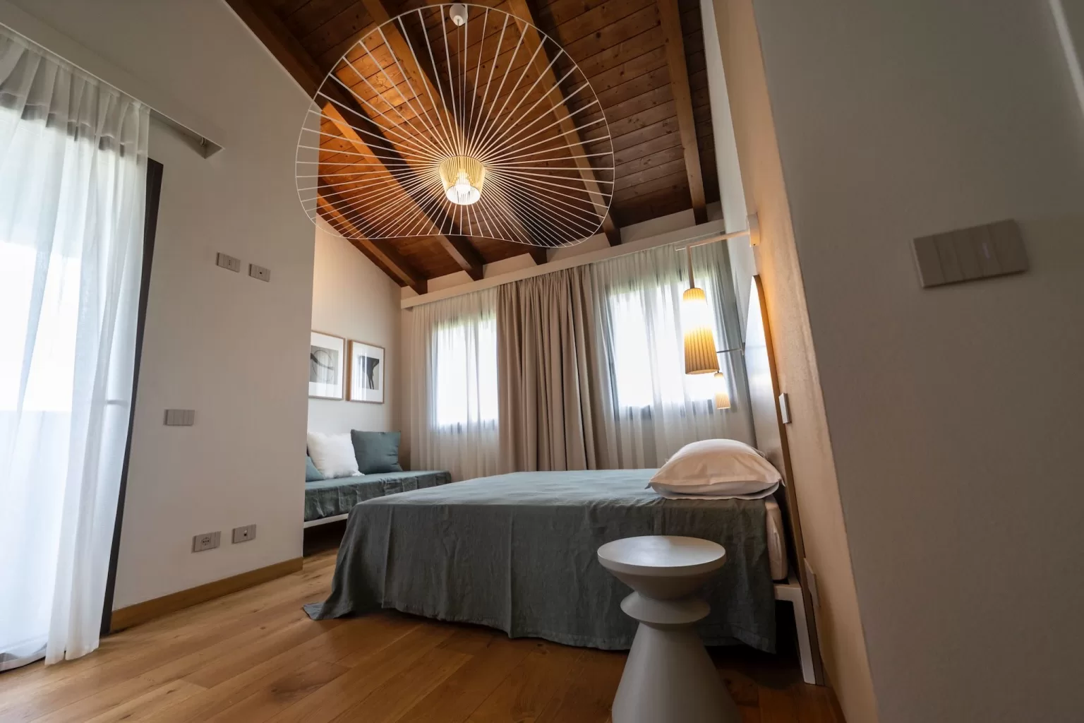 Contemporary bedroom at Villa Agavi with wooden ceilings, soft drapes, and sculptural lighting creating a peaceful retreat.