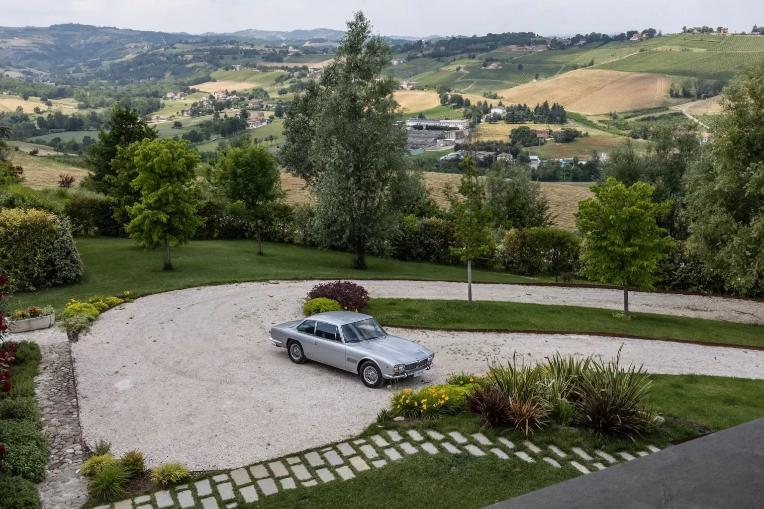 A silver vintage car parked in the circular driveway of Villa Agavi, surrounded by rolling Italian countryside.