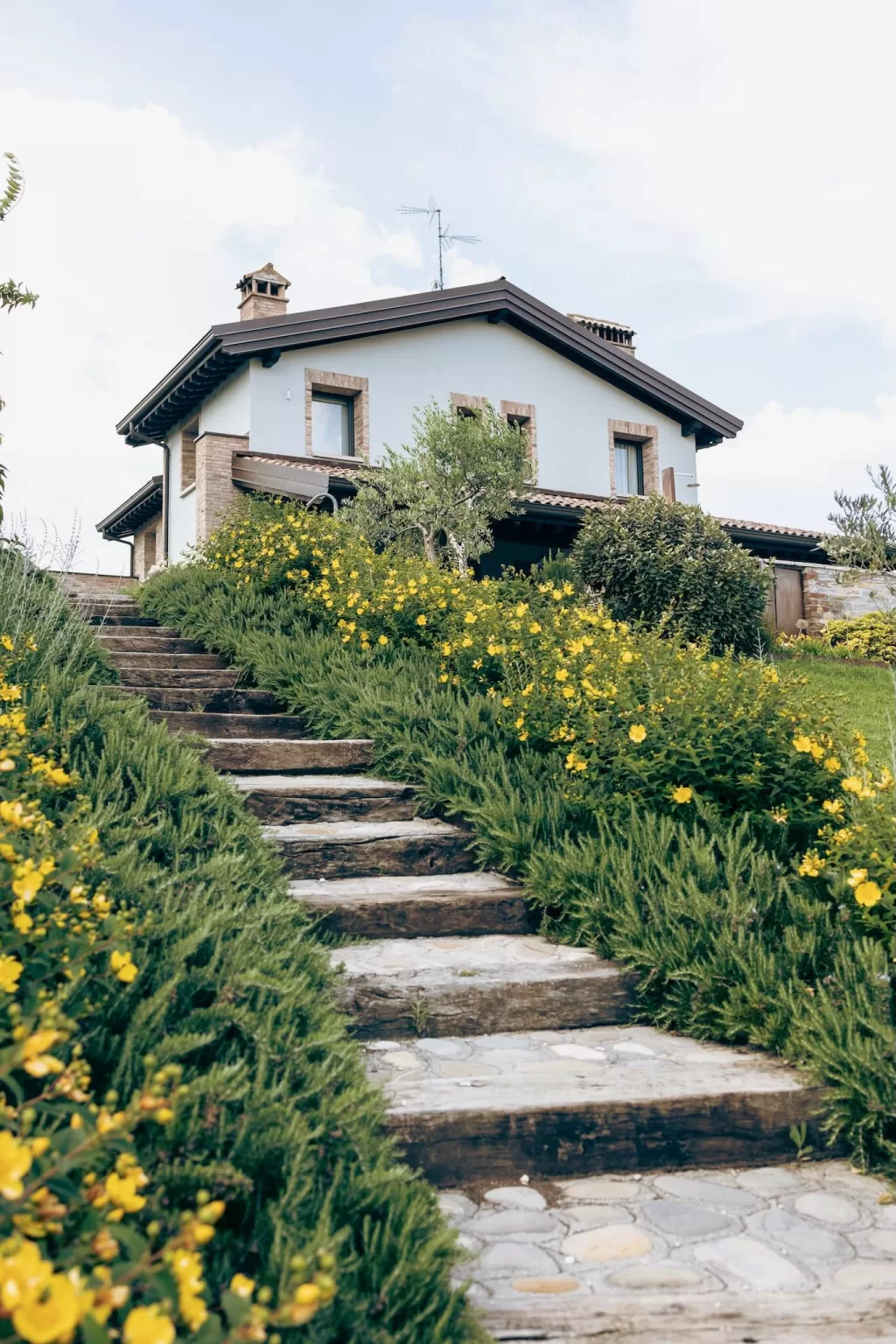 Stone steps lined with yellow blooms lead up to the entrance of Villa Agavi, nestled among lush Mediterranean gardens.