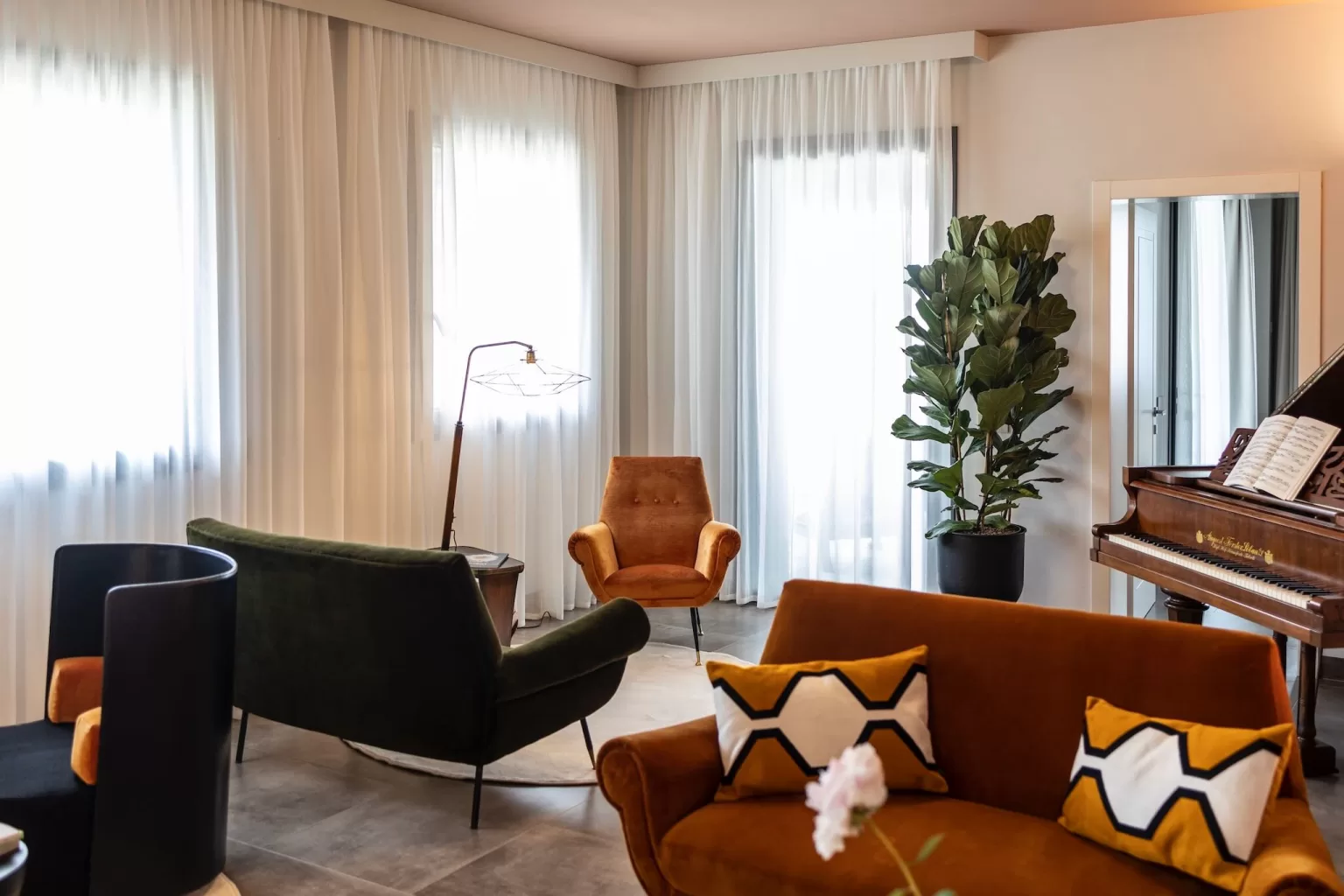 Stylish lounge area at Villa Agavi featuring rich velvet seating, a grand piano, and floor-to-ceiling curtains.