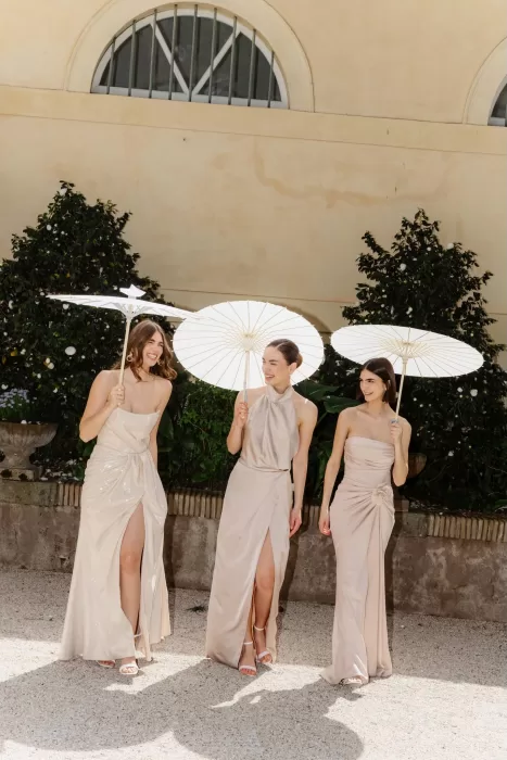 Bridesmaids in champagne dresses laughing under white parasols at Villa Aurelia
