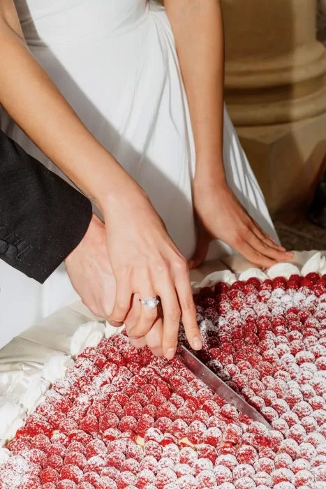 Close-up of bride and groom cutting raspberry-topped wedding cake together