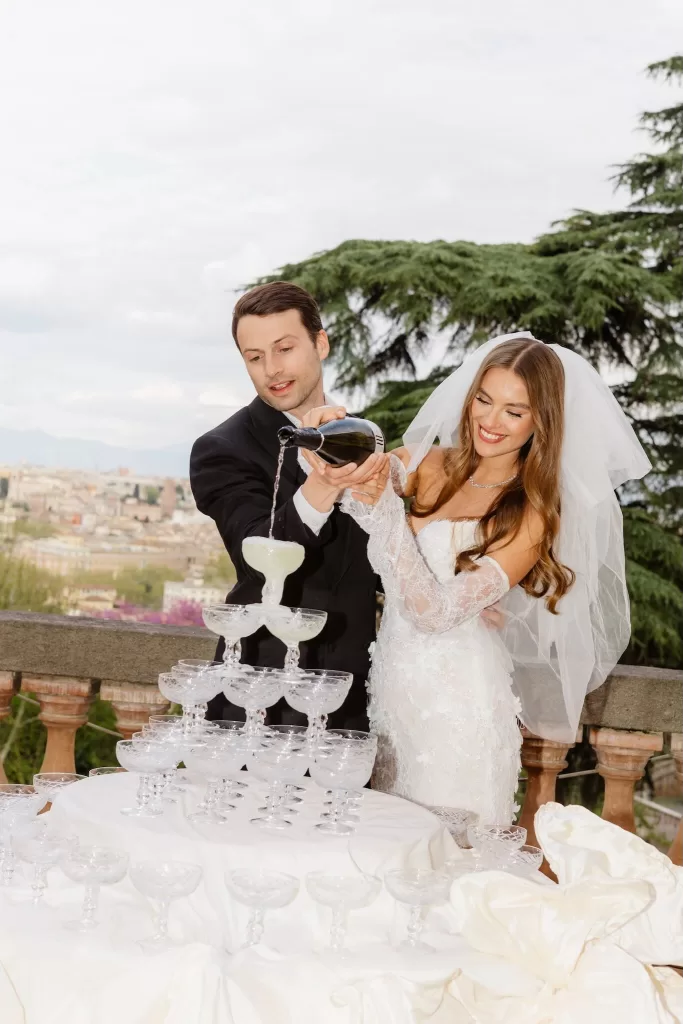 Bride and groom pouring champagne into a glass tower on the Villa Aurelia terrace