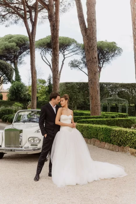 The couple poses beside a vintage Rolls-Royce in the elegant gardens of Villa Aurelia.