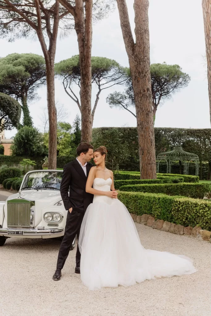 The couple poses beside a vintage Rolls-Royce in the elegant gardens of Villa Aurelia.