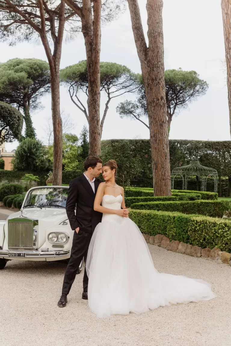 The couple poses beside a vintage Rolls-Royce in the elegant gardens of Villa Aurelia.