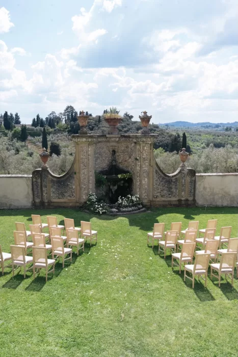 Elegant outdoor wedding ceremony setup facing a historic stone fountain with Tuscan hills in the background at Villa Medicea di Lilliano.