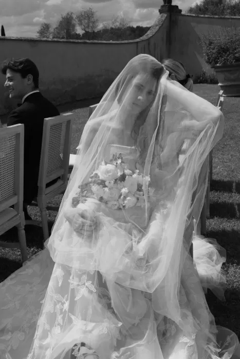 A bride sits beneath her veil holding a white bouquet, with soft sunlight filtering through at Villa Medicea di Lilliano.