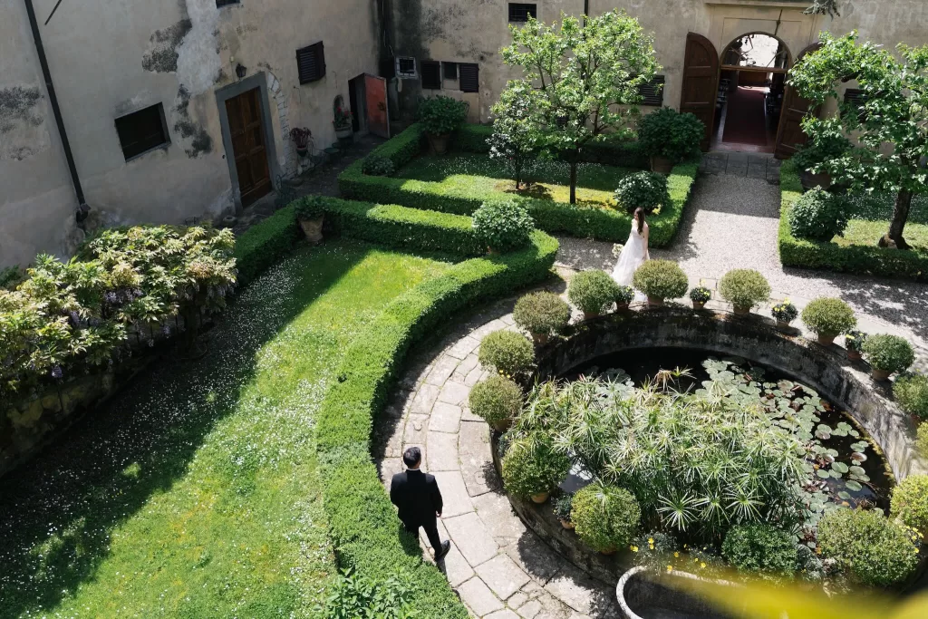 Aerial view of the bride and groom in the formal garden courtyard at Villa Medicea di Lilliano, surrounded by lush hedges and a lily pond.