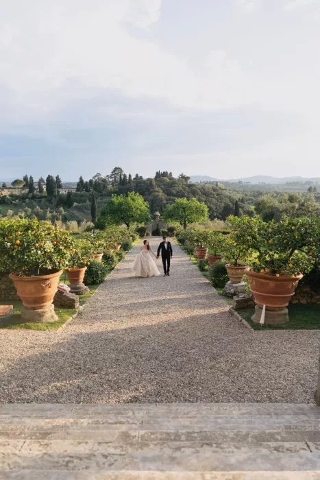 Bride and groom walking hand in hand through the lemon garden at Villa Medicea di Lilliano with rolling hills behind them.