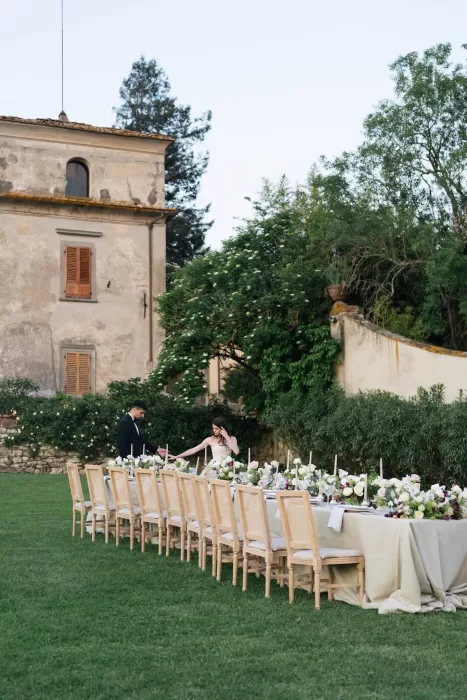Long floral wedding reception table set on the lawn, framed by rustic walls and greenery at Villa Medicea di Lilliano.