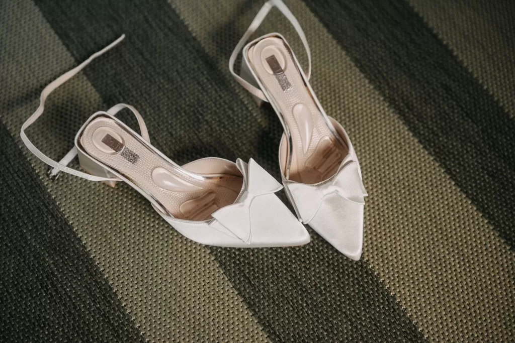Close-up of elegant satin bridal heels with bows resting on striped green carpet.