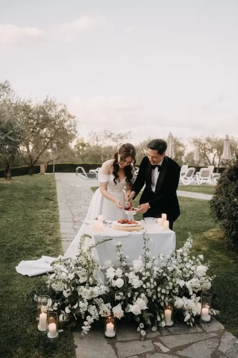 Bride and groom cutting a strawberry tart surrounded by white flowers and candles at Villa Olimpia.