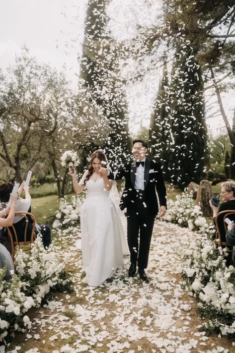 Just married couple walk through a shower of white confetti down the floral aisle at Villa Olimpia