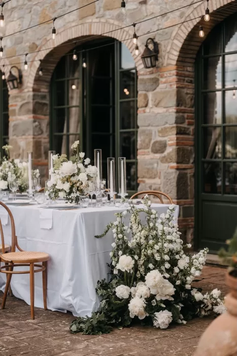 Elegant wedding reception table at Villa Olimpia with white flowers, tall candles, and string lights against a rustic stone wall.
