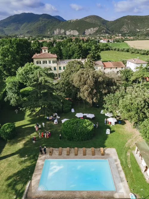 Aerial view of Villa Ravano with lush gardens, pool, and Tuscan hills in the distance.