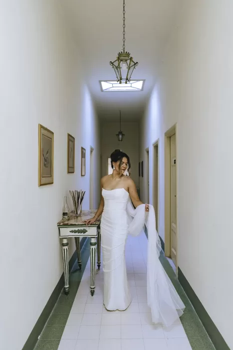 Bride stands alone in a quiet hallway at Villa Ravano, holding her veil with graceful poise.